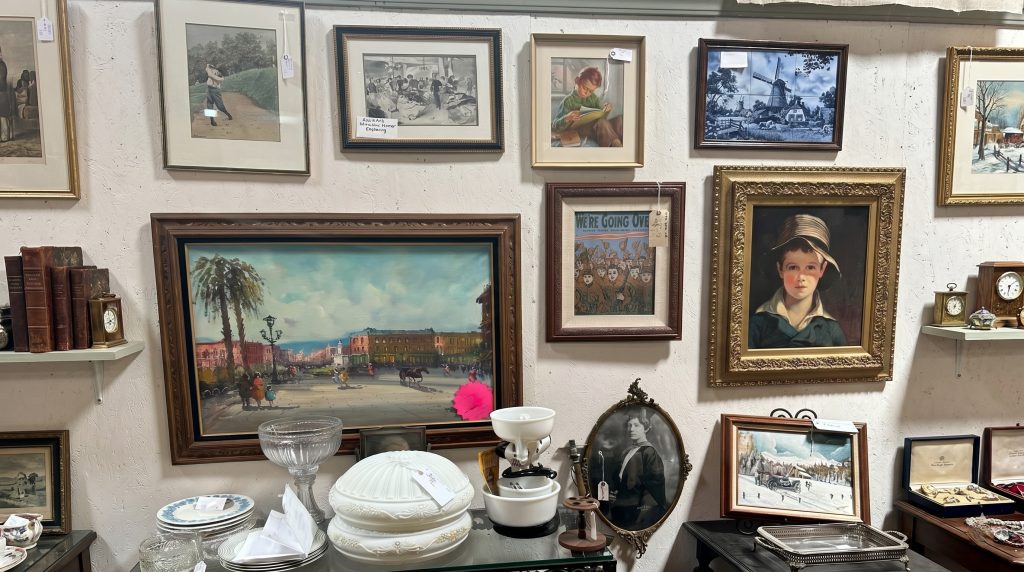 A curated display of antique framed paintings, vintage art prints, and collectible glassware inside Antique Harvest in Healdsburg, CA.